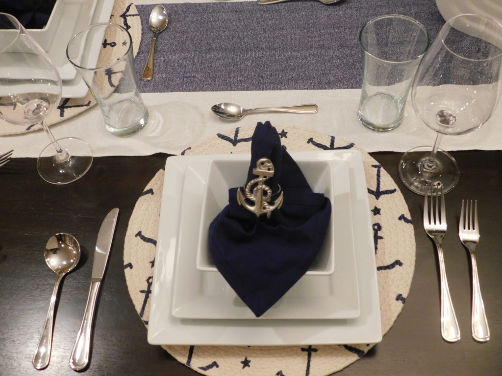 picture of table setting with nautical theme in blue and white. blue napkin and anchor napkin ring