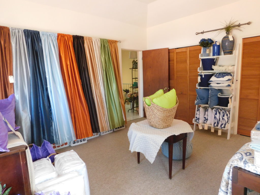 picture of all the textiles at the store showing curtains in different colours and a showcase of navy blue and white pillows , baskets and vases