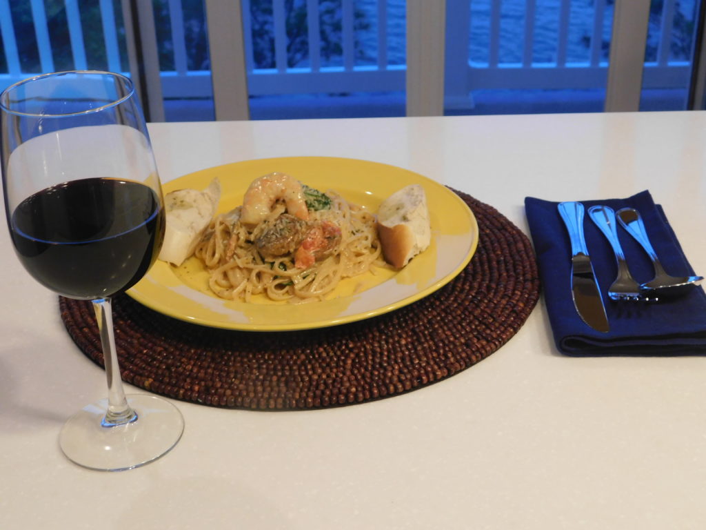 pasta on a yellow plate with utensils and a glass of wine.