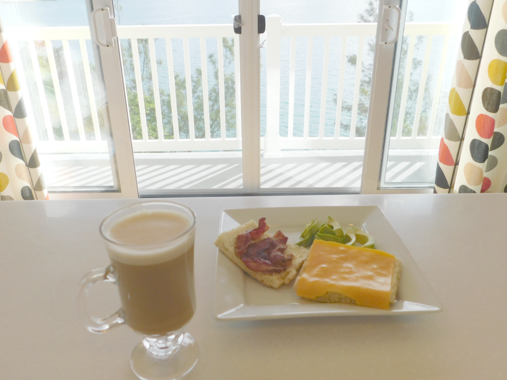 johnny bread with cheese avocado and bacon on a white plate with a latte on the side