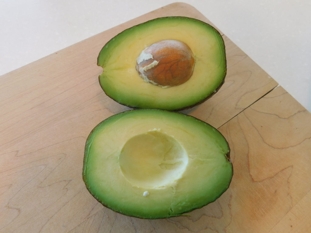 cutting board showing an avocado pear cut open