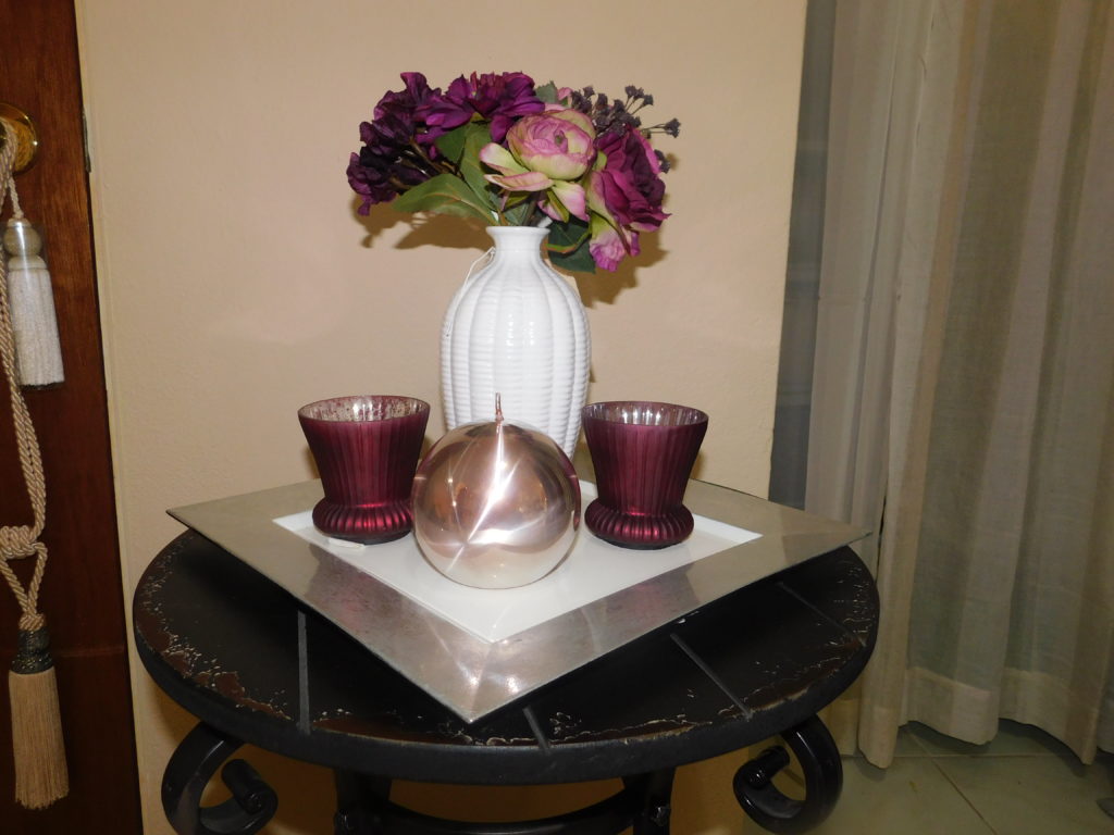 charger plate displaying purple votive holders a white vase and purple flowers and a rose gold ball candle