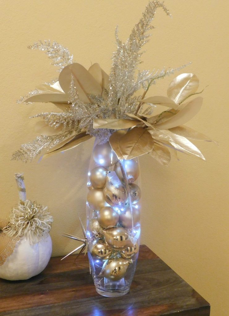 Tall vase containing gold christmas balls, led lights and gold and silver faux shrubery