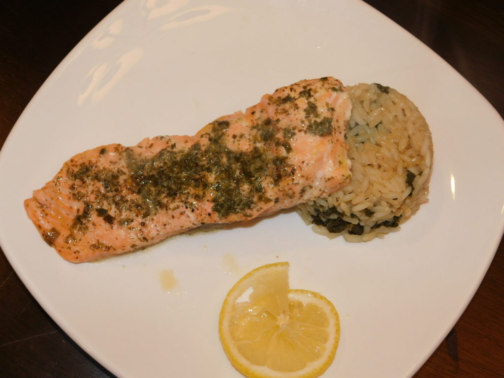 Baked salmon with kale and rice and a twist of lemon on a white plate